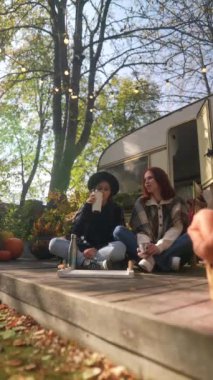 İki hippi kıyafetli kız sonbahar boyunca güneşli terasta sıcak çayın tadını çıkarıyorlar. Yüksek kalite 4k görüntü