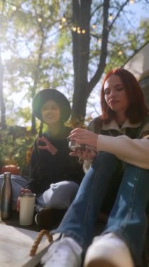 Moda ve hevesli iki kadın, tamamen hippi yaşam tarzına dalmış, sohbet ediyor ve karavanın yanındaki güzel sonbahar bahçesinde çaylarının tadını çıkarıyorlar. Yüksek kalite 4k görüntü