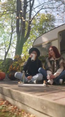 Güneşli bir sonbahar gününün tadını çıkaran hippi kızlar terasta sıcak çay yudumluyorlar. Yüksek kalite 4k görüntü