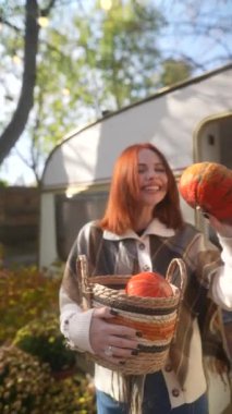 Sonbahar sezonunun tadını çıkaran bir kızıl saçlı, sonbahar bahçesinde bir sepet balkabağı sergiliyor. Yüksek kalite 4k görüntü