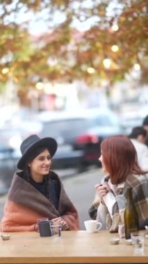 Güzelliklerini yayarak, şehirdeki sonbahar terasında çay eşliğinde birbirlerine bağlanan iki genç kadın. Yüksek kalite 4k görüntü
