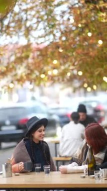İki modaya uygun ve genç kadın, şehrin cazibesine kendilerini tamamen kaptırmış, sonbahar terasında sohbet edip çay içiyorlar. Yüksek kalite 4k görüntü