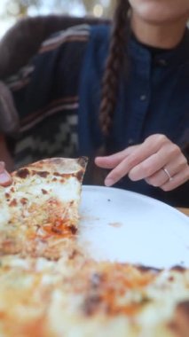 Havalı bir bayan, tamamen açık hava yemek deneyimine dalmış, sonbahar terasında pizzasının tadını çıkarıyor. Yüksek kalite 4k görüntü