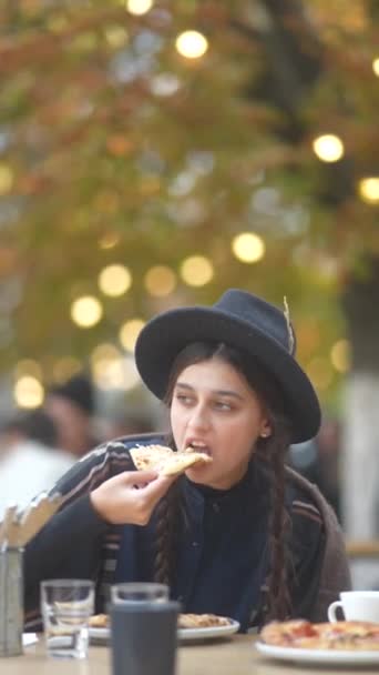 秋の衣装の美しい女の子が屋外テラスでピザを食べています 高品質の4K映像 — ストック動画