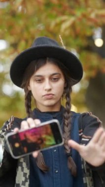 Sonbahar şehri sokaklarında şık bir kız şapkalı ve hippi kıyafetleriyle selfie çekiyor. Yüksek kalite 4k görüntü