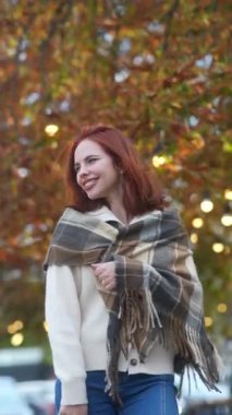 Sonbahar kıyafetleri içinde, yürekten kızıl saçlı bir kız şehrin sokaklarında dolaşıyor. Yüksek kalite 4k görüntü