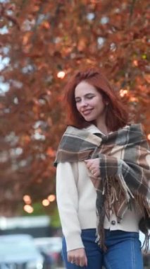 Sonbahar kıyafetleri içinde, yürekten kızıl saçlı bir kız şehrin sokaklarında dolaşıyor. Yüksek kalite 4k görüntü