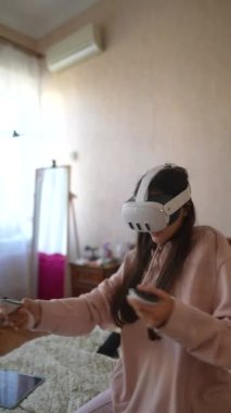 Pembe pijama giymiş sevimli genç bir bayan sanal gerçeklik kulaklığıyla video oyunlarından hoşlanıyor. Yüksek kalite 4k görüntü