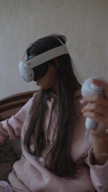 Kararlı bir kadın kendi evinde video oyunlarından zevk alarak VR kulaklığı kullanıyor. Yüksek kalite 4k görüntü