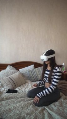 Canlı bir genç kadın, VR kulaklığıyla evinde yatağında uzanırken video oyunu oynuyor. Yüksek kalite 4k görüntü