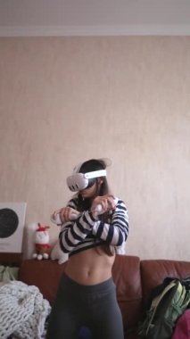 Ev ortamında, genç ve güzel bir bayan kendini video oyununa bir VR kulaklığının yardımıyla sokuyor. Yüksek kalite 4k görüntü