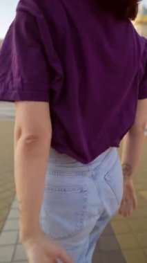 Güneşli bir günde, genç kızıl saçlı bir kadın kulaklıkları kulağında güzel bir şekilde dans eder. Yüksek kalite 4k görüntü