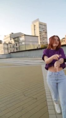 Kulaklık takan çarpıcı kızıl saçlı bir bayan şehir meydanında dans etmekten hoşlanıyor. Yüksek kalite 4k görüntü
