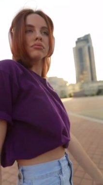 Kulaklık takan çarpıcı kızıl saçlı bir bayan şehir meydanında dans etmekten hoşlanıyor. Yüksek kalite 4k görüntü