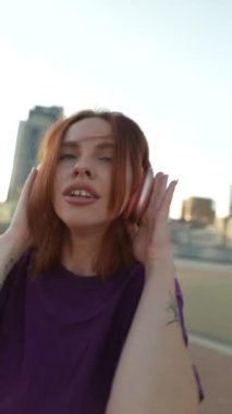 Şehir meydanının ortasında kızıl saçlı ve kulaklıklı güzel bir kız dans ediyor. Yüksek kalite 4k görüntü