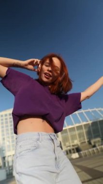 Şok edici kızıl saçlı, kulaklıklı kadın şehir meydanında dans ediyor. Yüksek kalite 4k görüntü