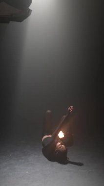 Loş bir odada, koyu renk elbiseli genç bir kız elinde bir ışık tutarak aktif olarak dans ediyor. Yüksek kalite 4k görüntü