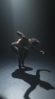 Loş bir odada, koyu renk elbiseli genç bir kız elinde bir ışık tutarak aktif olarak dans ediyor. Yüksek kalite 4k görüntü