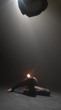 Loş bir salonda, koyu renk elbiseli genç bir bayan ışıkla enerjik bir şekilde dans ediyor. Yüksek kalite 4k görüntü