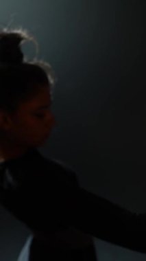 Çağdaş dansla meşgul olan genç kadın, karanlık stüdyoda zarafetle hareket ediyor. Yüksek kalite 4k görüntü