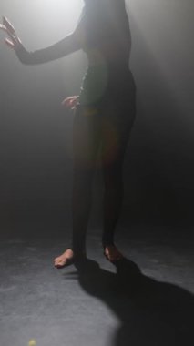 Karanlık bir stüdyoda, siyah giyinmiş güzel bir kız modern bir dans gösterisi sergiliyor. Yüksek kalite 4k görüntü