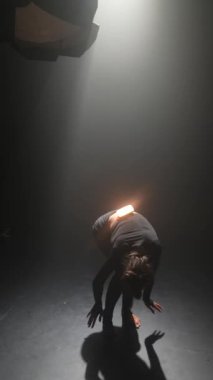 Karanlık bir stüdyoda, siyah elbiseli muhteşem bir kız modern bir dans gösterisi yapıyor. Yüksek kalite 4k görüntü