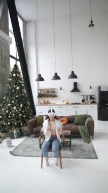 Güzel genç bir kadın Noel ağacına karşı sanal gerçeklik kulaklığıyla iletişim kuruyor. Yüksek kalite 4k görüntü