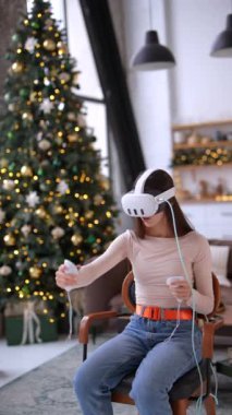 Noel süslemeli bir evde sanal gerçeklik kulaklığı takarak oyuna dalmış hoş bir genç bayan. Yüksek kalite 4k görüntü