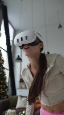 VR kulaklığı takan genç bir kadın, apartman dairesinde spor kıyafetleri içinde Noel ağacının yanında egzersiz yapıyor. Yüksek kalite 4k görüntü