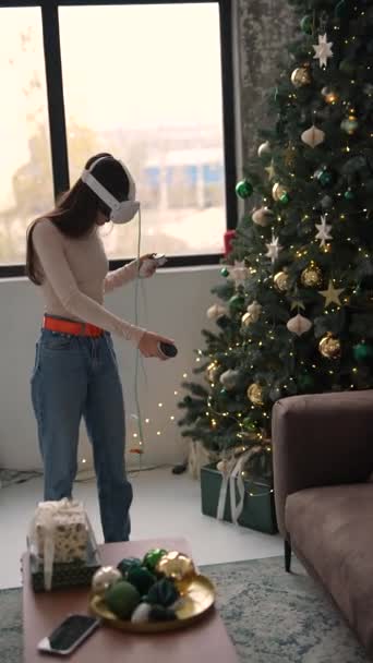 一个年轻的女人戴着一个虚拟现实的耳机站在圣诞树旁 她的情绪很活跃 高质量的4K镜头 — 图库视频影像