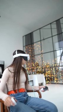 Şenlikli bir Yeni Yıl dairesi içinde, trend bir kız sanal gerçeklik kulaklığıyla çalışıyor. Yüksek kalite 4k görüntü