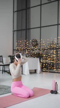Tarz sahibi genç bir kadın tatil tatilinde evde sanal gerçeklik kulaklığı kullanarak yoga yapıyor. Yüksek kalite 4k görüntü