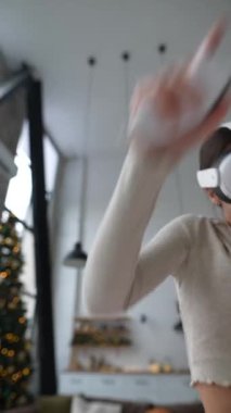 Sportif giyimli çekici bir kadın Noel hediyesi olarak aldığı sanal gerçeklik kulaklığını kullanarak hevesle video oyunu oynuyor. Yüksek kalite 4k görüntü