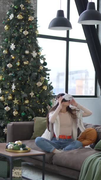 坐在圣诞树下 一个年轻漂亮的女人用一个虚拟现实耳机玩电子游戏 高质量的4K镜头 — 图库视频影像