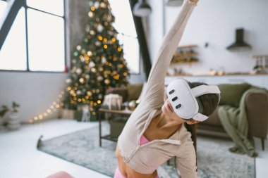 Yoga pozları veren zinde bir kadın Noel ağacının yanında sanal gerçeklik gözlüğü takıyor. Yüksek kalite fotoğraf