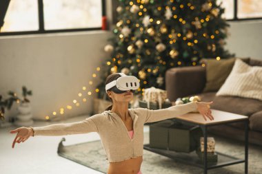 Sanal gerçeklik kulaklığı takan sportif, modaya uygun bir kadın bir Noel ağacının yanında yoga pozları veriyor. Yüksek kalite fotoğraf
