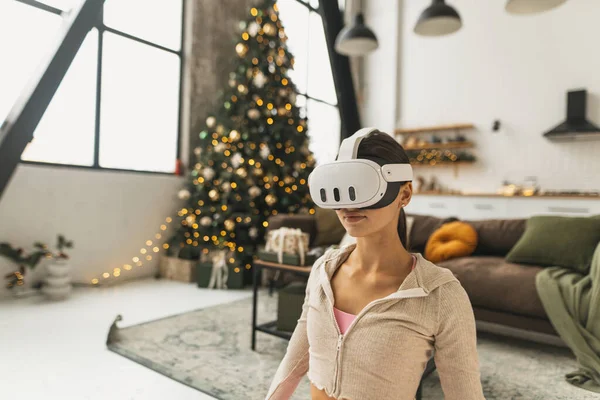 一名年轻女子在圣诞树旁使用虚拟现实眼镜 展示瑜伽姿势 高质量的照片 — 图库照片