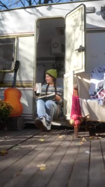 Güz bahçesindeki karavan terasında gitarı ve sıcak içeceği olan şık, genç bir hippi kız. Yüksek kalite 4k görüntü