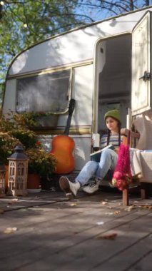 Güz bahçesindeki karavan terasında gitarı ve sıcak içeceği olan şık, genç bir hippi kız. Yüksek kalite 4k görüntü