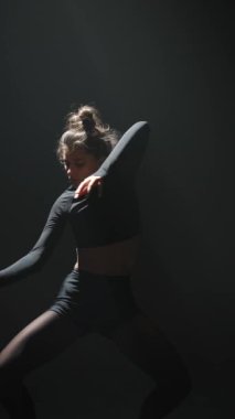 Koyu renk elbiseli güzel bir bayan loş bir stüdyoda çağdaş bir dans gösterisi yapıyor. Yüksek kalite 4k görüntü