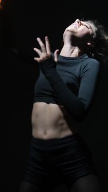 Siyah giyinmiş güzel bir kadın loş bir stüdyoda modern bir şekilde dans ediyor. Yüksek kalite 4k görüntü