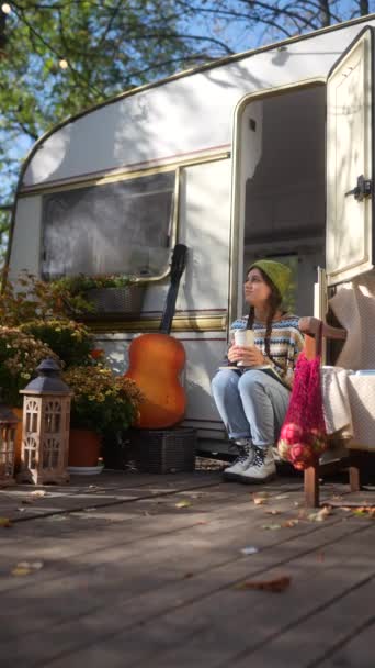 在秋天的花园 一个时髦的年轻嬉皮士女孩 带着吉他和热饮料坐在拖车的阳台上 高质量的4K镜头 — 图库视频影像