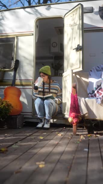 一个时髦的 年轻的嬉皮士女孩 带着吉他和热饮在秋天花园的拖车平台上 高质量的4K镜头 — 图库视频影像