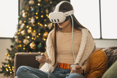 Evinde rahat bir Noel atmosferiyle çevrili şık genç bir kadın sanal gerçeklik kulaklığı takıyor. Yüksek kalite fotoğraf