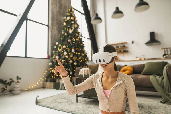 在圣诞节假期里 一个时髦的年轻女人用一个虚拟现实耳机 高质量的照片 — 图库照片
