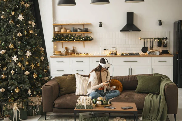 在她家里温暖的圣诞氛围中 一个时髦的年轻女人出现在一个虚拟现实的耳机里 高质量的照片 — 图库照片