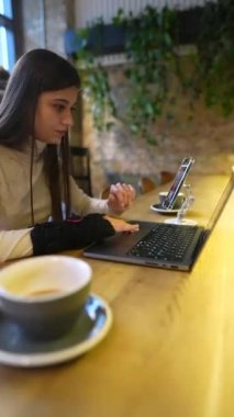 Tıp okuyan genç bir öğrenci bir kafede internetten öğreniyor, hem telefon hem de dizüstü bilgisayar kullanıyor. Yüksek kalite 4k görüntü
