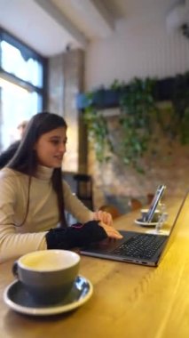 Bir kafede, genç ve sevimli bir öğrenci dizüstü bilgisayarla oturur ve biriyle konuşur. Yüksek kalite 4k görüntü