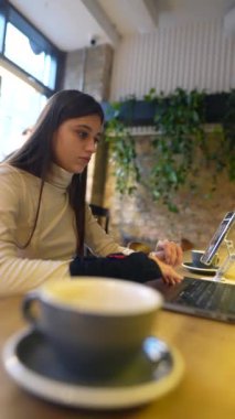 Genç ve güzel bir öğrenci bir kafede oturuyor, bir dizüstü bilgisayarla sohbet ediyor. Yüksek kalite 4k görüntü