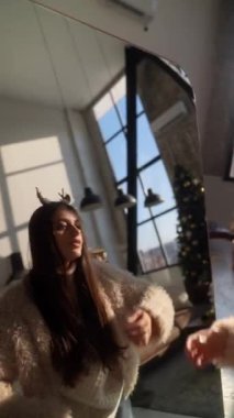 Evde, genç ve güzel bir kadın aynanın önünde Noel geyiği maskesi deniyor. Yüksek kalite 4k görüntü